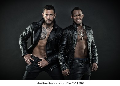 Two Male Models Posing Together. Desire And Seduction Concept. African Guy With Joyful Smile. Hispanic Man With Geometrical Tattoo On Hairy Chest. Bodybuilders Wearing Leather Jackets On Bare Torsos.