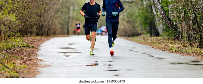 two male runners run race on wet road in forest