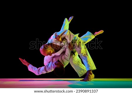 Two male sportsmen, martial arts fighters in white kimono fighting performing techniques in motion in neon light isolated black background. Concept of combat sport, energy, fit. Copy space, ad