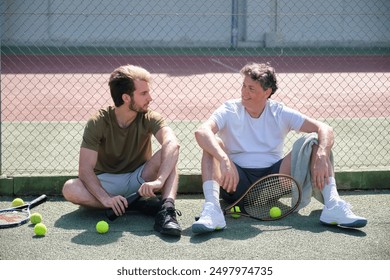 Two male tennis players taking a break from their tennis match, having a friendly conversation on the court - Powered by Shutterstock