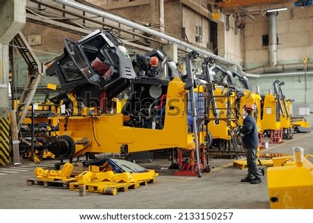 Two male workers of modern industrial plant or repairmen checking efficiency of huge construction machines in workshop