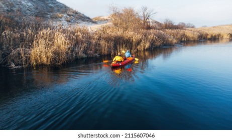 Two Man In Bright Clothes Floats On A Red Kayak On The River. Winter. Ukraine