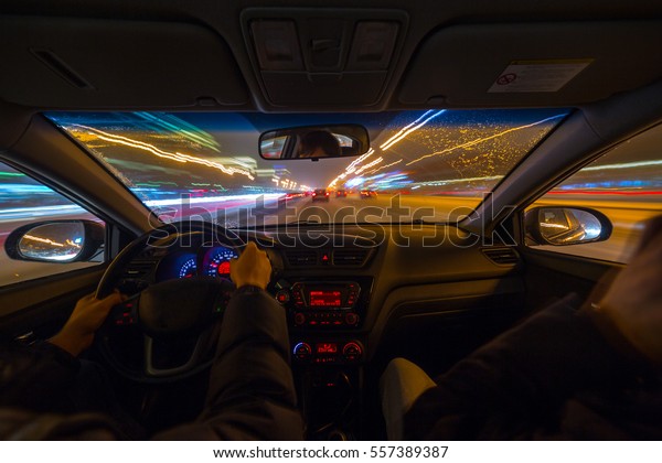 Two man in a car moves at\
fast speed at the night. Blured road with lights with car on high\
speed.
