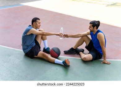 Two man friends athlete resting and drinking water together after play streetball on outdoors court in sunny day. Sportsman basketball player do sport training workout at street court in the city. - Powered by Shutterstock