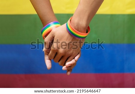 Two man holding hands with a rainbow-patterned wristband on their wrists with the LGBTQ rainbow flag in the background. lgbt, same-sex relationships and homosexual concept