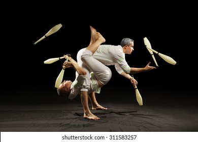 Two man juggling clubs isolated black background 