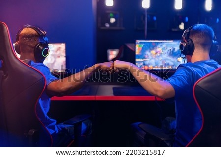 Two man professional cyber sport gamers giving fist hand bump, back view. Concept winner eSports tournament. Neon color soft focus.