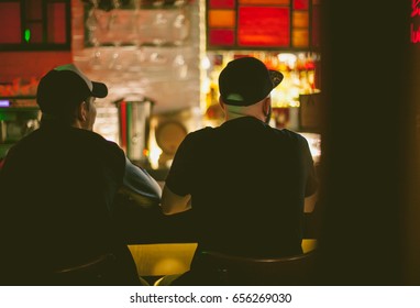 Two man are sitting at the bar counter, back to the camera. Attractive two young guys are drinking beer in a bar.They are sitting, they are smiling. Friends in the bar. soft focus vintage toning photo