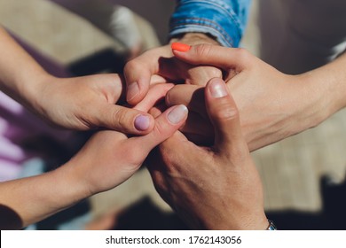 two man and three women holding hands on a table implying a polyamory relationship or love triangle.