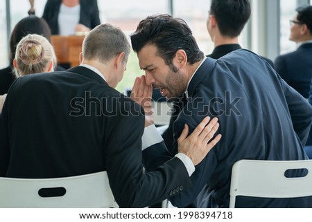 two man whispering while sitting in audience at conference room