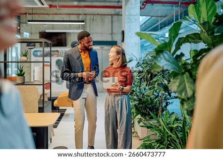Two managers walking through a modern green office, discussing project details while using a tablet in a bright, airy workspace