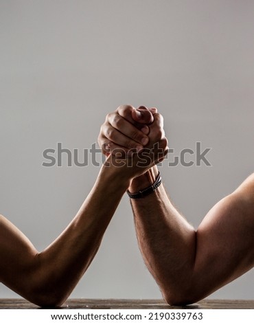 Two man's hands clasped arm wrestling, strong and weak, unequal match. Heavily muscled man arm wrestling a puny weak man.