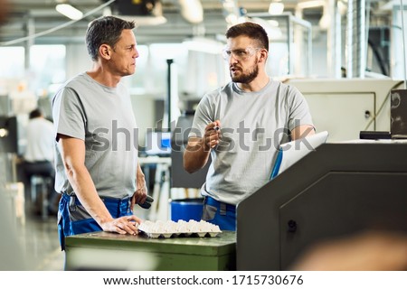 Two manual workers talking while working in a industrial facility. 