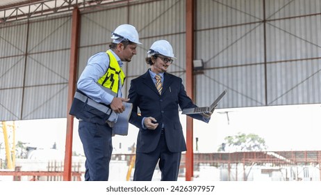 Two manufacturing engineers using computer notebook to check production system in construction factory. Factory owner and his civil engineer using laptop to design production and management systems.