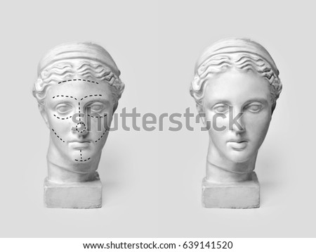 Two marble heads of young women, ancient Greek goddess bust marked with lines for plastic surgery and sculpture after operation on light background. Old and new beauty standarts concept.