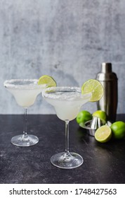 Two Margarita Cocktails With Limes And Shaker On Black Counter