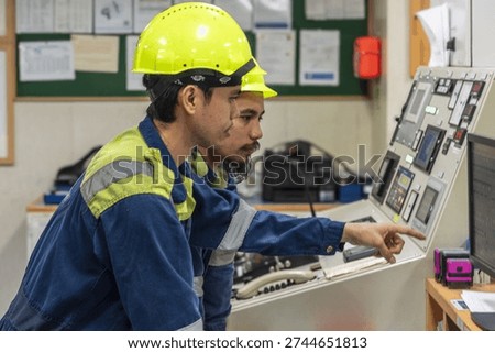 Two marine engineers operating control panels inside ship engine control room during routine monitoring.