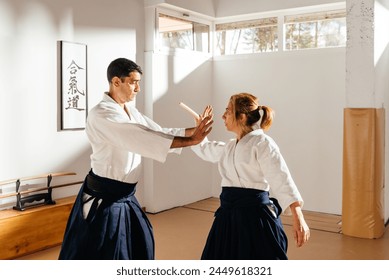 Two martial artists, one executing a knife defense move, practice martial arts in a dojo with sunlight streaming through the windows (Text meaning: "Aikido"). - Powered by Shutterstock