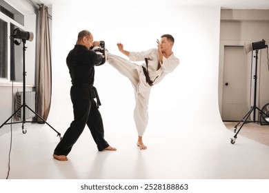 Two martial artists practicing karate, one in a white gi and the other in a black gi. The man in white strike delivers a while the other holds a hand makiwara for training. - Powered by Shutterstock