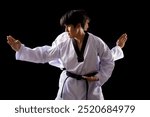 Two martial artists wearing white taekwondo uniform demonstrates defensive stance against dark background