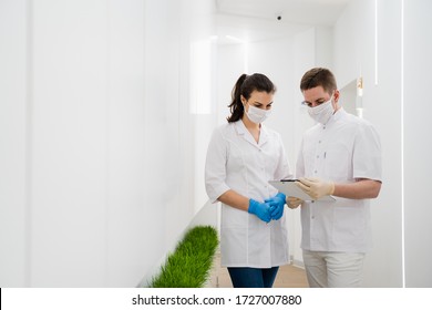 Two masked doctors read medical documents and discuss the diagnosis of a patient in a modern hospital during the quarantine pandemic
