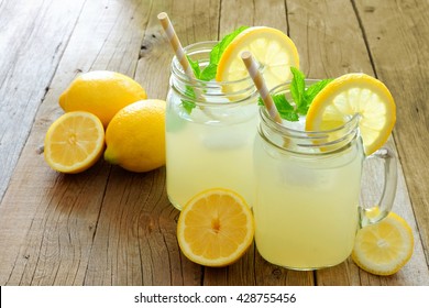 Two mason jar glasses of homemade lemonade on a rustic wooden background