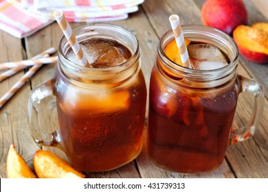 Two mason jar glasses of homemade peach iced tea on a rustic wood background