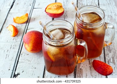 Two mason jar glasses of homemade peach iced tea on a rustic white wood background
