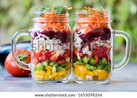 Two mason jars packed with colourful layered fresh vegetable salad to bring to work