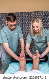 Two Massage Therapists A Woman And A Ma Give A Double Foot And Leg Massage To A Girl In A Spa Salon. Four Hands Of Masseur During Massage Close Up