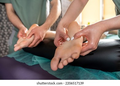 Two Massage Therapists, A Woman And A Man, Give A Double Foot And Leg Massage To A Girl In A Spa Salon. Four Hands Of Masseur During Massage Close Up. Spa Salon