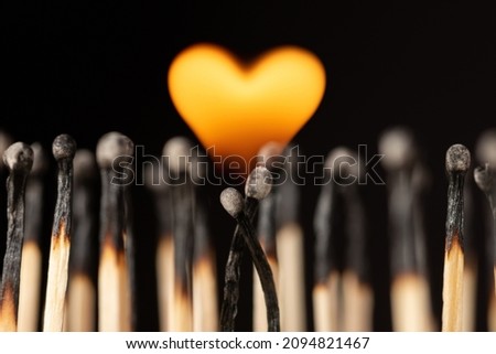 Two matches hanging each other and burning with flame in shape of a heart. Concept of love