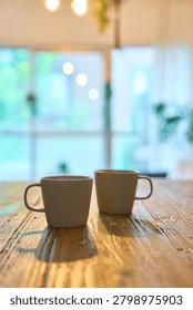 Two matching ceramic mugs side by side on rustic wooden table with soft natural light and blurred background