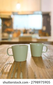 Two matching ceramic mugs side by side on rustic wooden table with soft natural light and blurred background