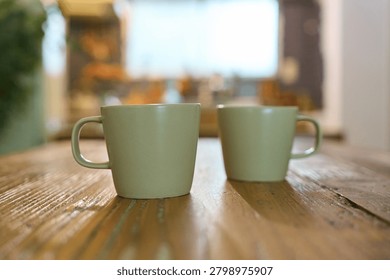 Two matching ceramic mugs side by side on rustic wooden table with soft natural light and blurred background