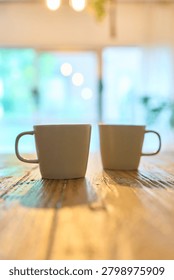 Two matching ceramic mugs side by side on rustic wooden table with soft natural light and blurred background