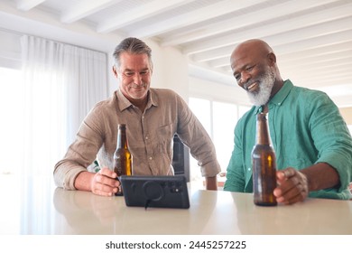 Two Mature Male Friends At Home Drinking Beers And Watching Sports On Mobile Phone - Powered by Shutterstock