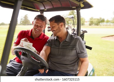 Two Mature Men Playing Golf Marking Scorecard In Buggy Driving Along Course - Powered by Shutterstock