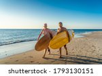 Two mature men walking with surfboards on beautiful beach enjoying paradise and retirement lifestyle. Attractive fit senior adults friends having fun surfing. In real active and healthy people.