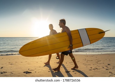 Two Mature Men Walking With Surfboards On Beautiful Beach Enjoying Paradise And Retirement Lifestyle. Attractive Fit Senior Adults Friends Having Fun Surfing. In Real Active And Healthy People.