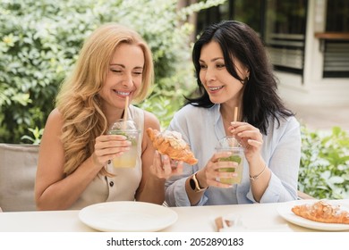 Two Mature Middle-aged Caucasian Girlfriends Best Friends Women Having Breakfast Brunch Together In City Cafe, Talking Gossiping Sharing News. Friendship Concept