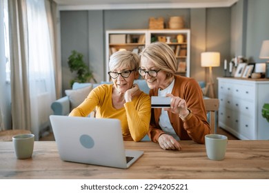 two mature senior women grandmother females sit at home use credit or debit card for online shopping browse internet stores buying stuff use digital tablet real people copy space - Powered by Shutterstock