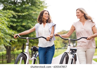 Two mature women in conversation while walking with bicycle at park. Happy beautiful senior women walking in the park with bicycles in a spring time. Friends holding bikes and talking to each other.
 - Powered by Shutterstock