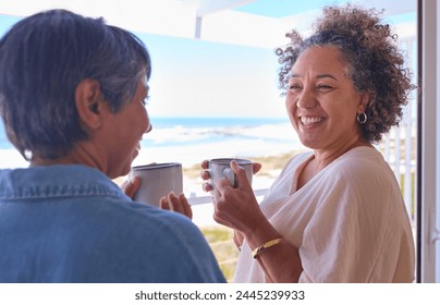 Two Mature Women Friends In Beachfront House Overlooking Ocean For Summer Vacation With Hot Drinks - Powered by Shutterstock