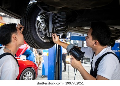 Two Mechanic Was Checking The Car Suspension. Vehicle Raised On Lift At Maintenance Station. Car In Service Station With Two Men Repair. Car Mechanic Working At Automotive Service Center.