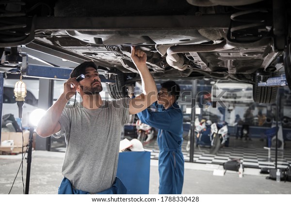 Two\
mechanic was checking the car suspension. Vehicle raised on lift at\
maintenance station. Car in service station with two men repair.\
Car mechanic working at automotive service\
center.