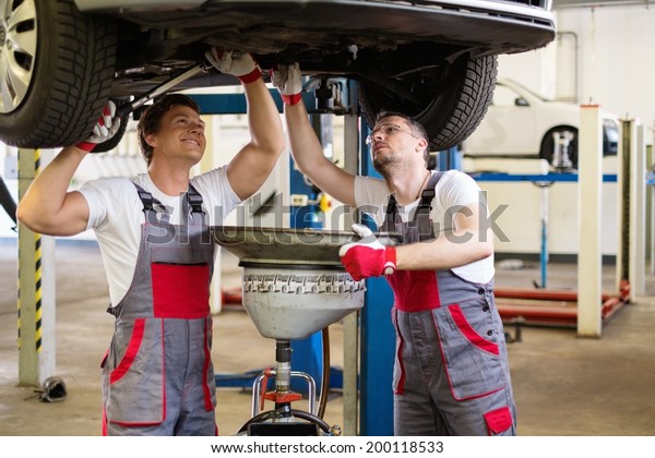 Two mechanics\
changing oil  in a car\
workshop
