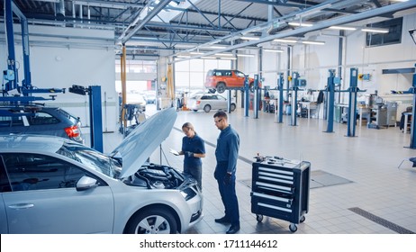 Two Mechanics in a Service are Inspecting a Car After They Got the Diagnostics Results. Female Specialist is Comparing the Data on a Tablet Computer. Repairman is Using a Ratchet to Repair the Faults. - Powered by Shutterstock