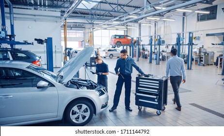 Two Mechanics in a Service are Inspecting a Car After They Got the Diagnostics Results. Female Specialist is Comparing the Data on a Tablet Computer. Repairman is Using a Ratchet to Repair the Faults. - Powered by Shutterstock