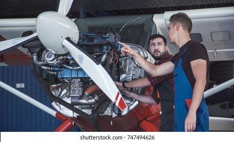 Two mechanics working on a small aircraft in a hangar with the cowling off the engine as they perform a service or repair - Powered by Shutterstock